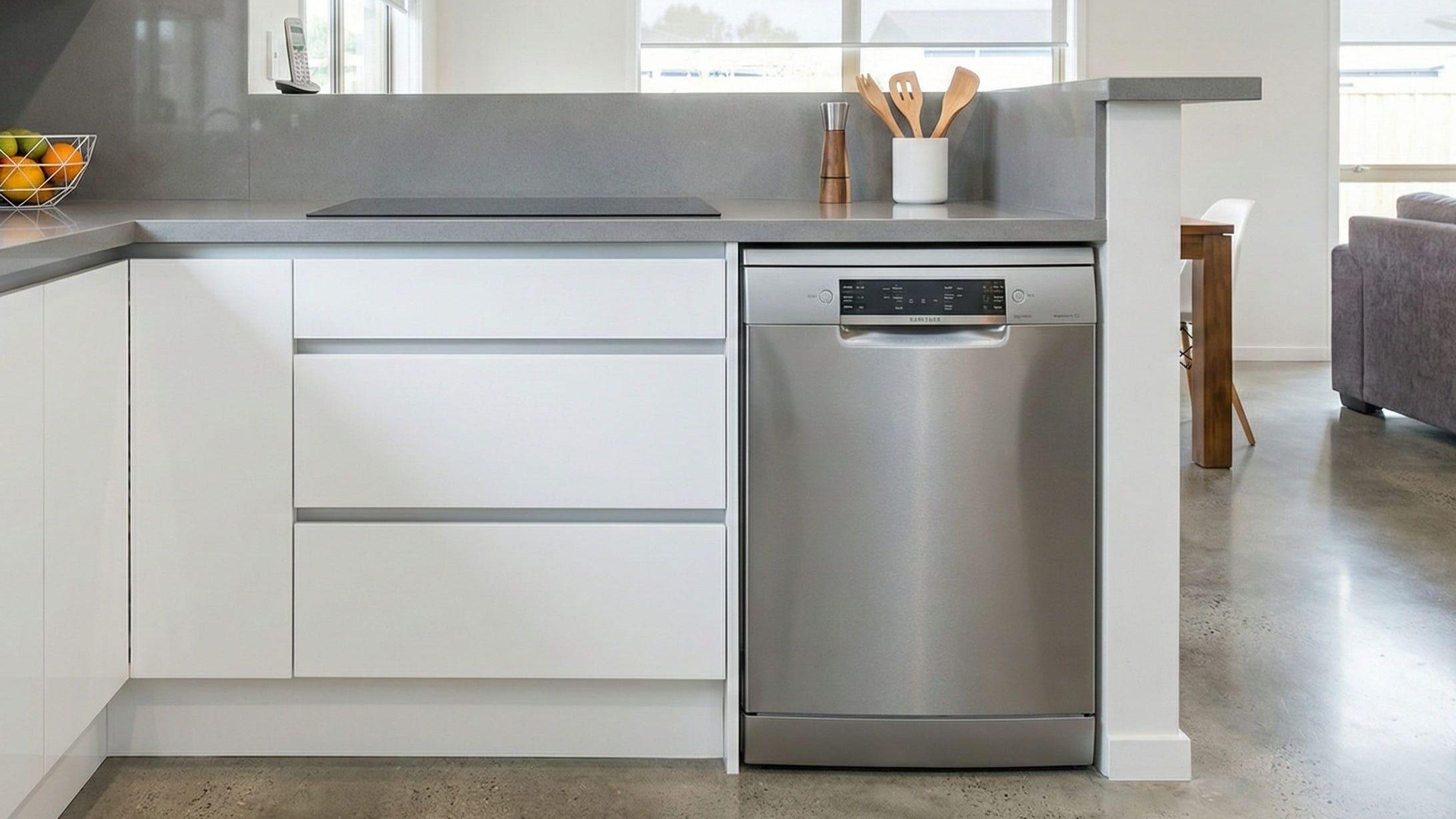 Freistehender Geschirrspüler in Edelstahloptik neben hellen Küchenzeilen mit grauer Arbeitsplatte.